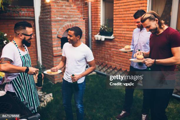 amigos en una barbacoa en el patio trasero - male burger eating fotografías e imágenes de stock