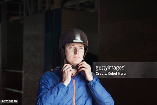 man fastening the belt of a helmet and preparing for horse riding - jockey foto e immagini stock