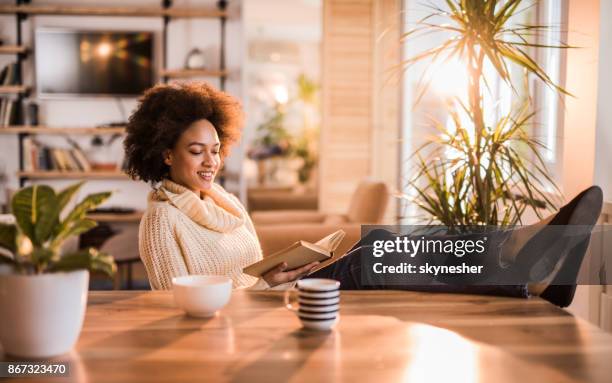 young happy african american woman relaxing with a book at home. - feet up stock pictures, royalty-free photos & images