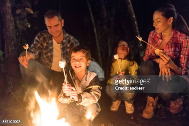 family sitting outdoors by a bonfire eating marshmallows - marshmallow stock pictures, royalty-free photos & images
