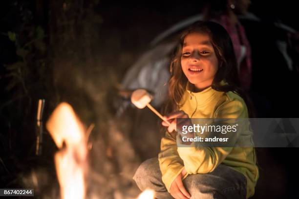 fille heureuse, assis à l’extérieur par un feu en mangeant des guimauves - camping kids photos et images de collection