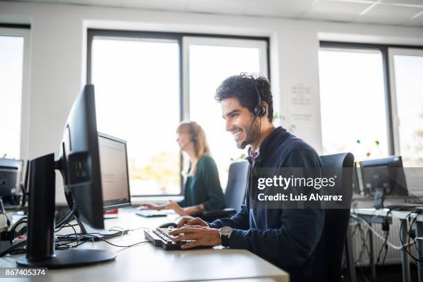 smiling customer service representative using computer at desk - freisprechanlage stock-fotos und bilder