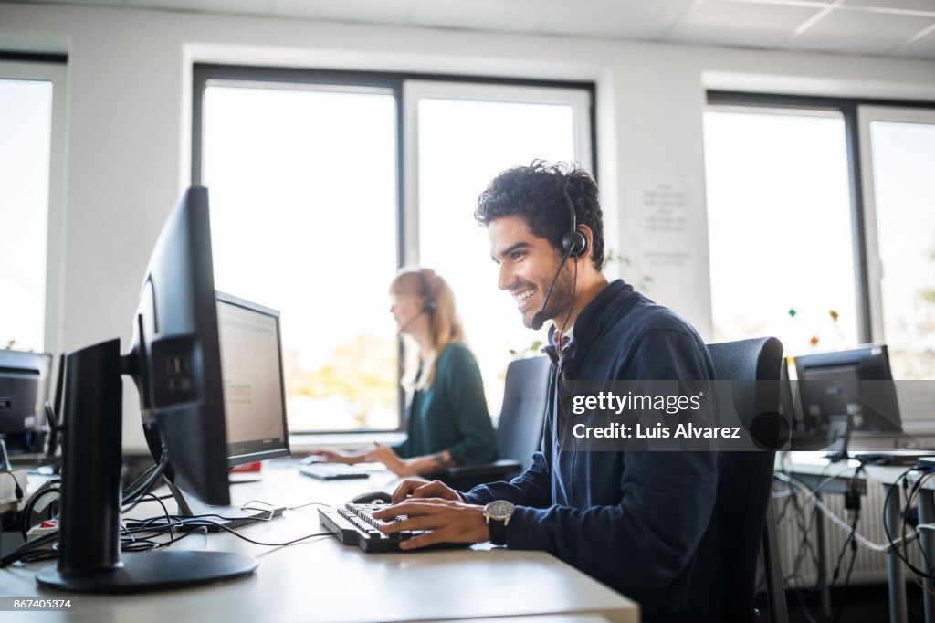 Smiling customer service representative using computer at desk