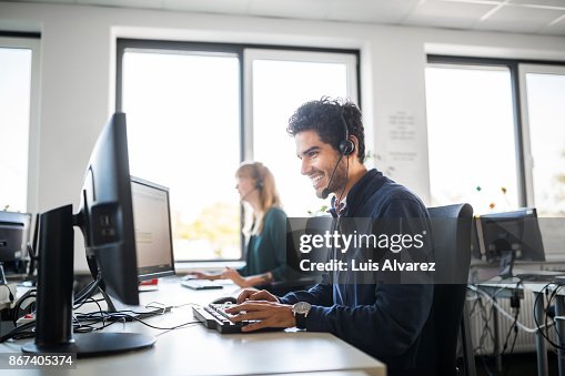 Smiling customer service representative using computer at desk Smiling customer service representative using computer at desk