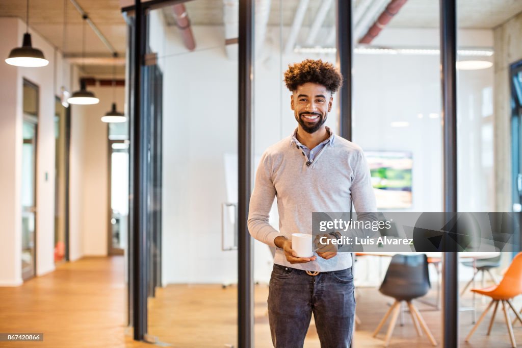 Smiling businessman holding coffee cup in front of board room