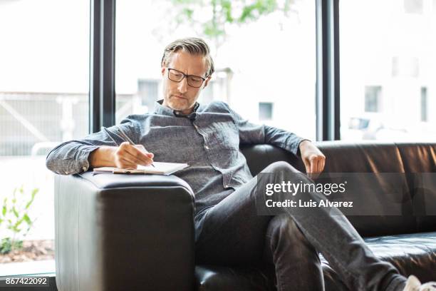 confident businessman writing on clipboard in creative office - ceo fotografías e imágenes de stock