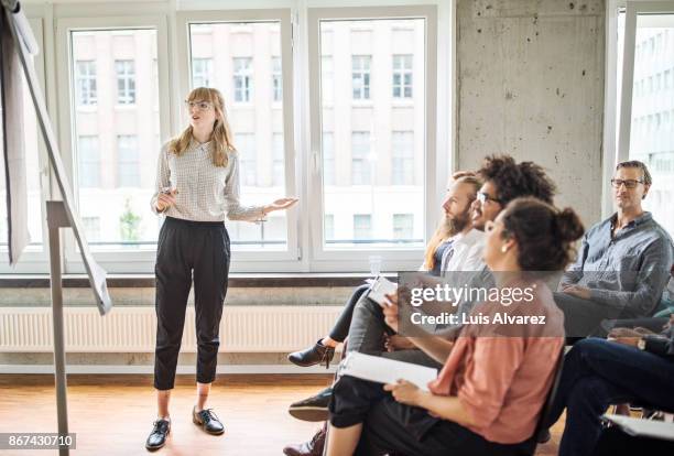 confident businesswoman giving presentation to coworkers - casual business meeting stock-fotos und bilder