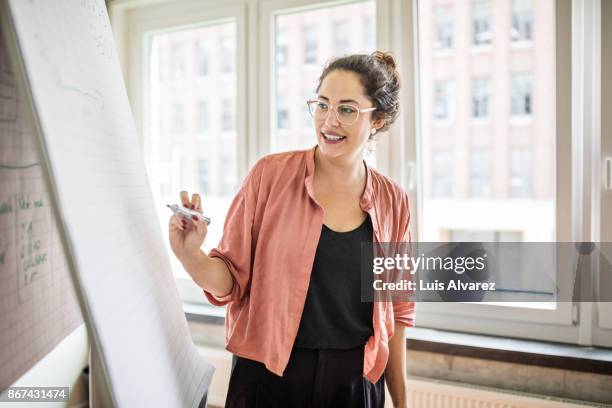 confident businesswoman giving presentation in creative office - woman whiteboard fotografías e imágenes de stock