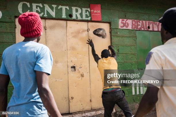 Man throws a stone as a mob attempts to break down the door of a shop in Kawangware, on October 28 as violence broke out following a disputed...