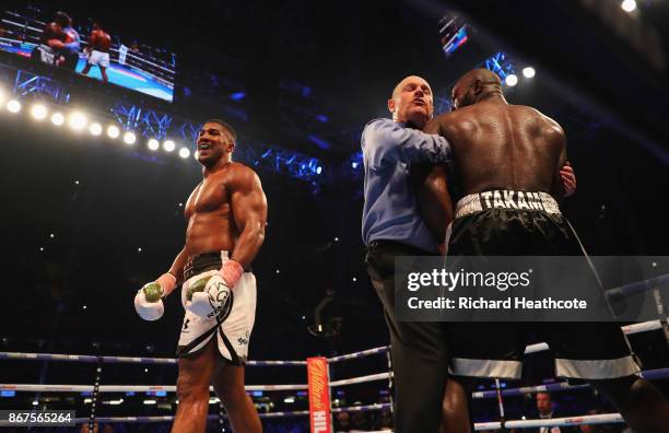 Anthony Joshua looks on as referee Phil Edwards holds Carlos Takam as he stops the fight in the 10th round during the IBF, WBA & IBO Heavyweight...