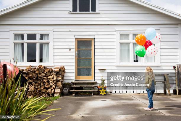 girl stands in front of a bungalow holding colourful balloons - nz house and driveway stock-fotos und bilder