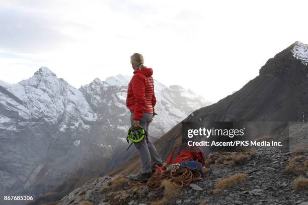mountaineer looks out to mountains from summit, with gear - puffer jacket stock pictures, royalty-free photos & images