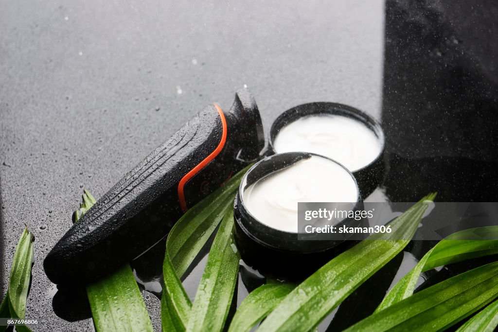 Electronic shaving with cream aftershave on green leaves and wet background