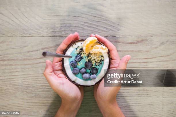 guy eating healthy breakfast food in the morning on wood table inside coconut with yogurt, fruit and cereals taken directly from above. - trying new food stock pictures, royalty-free photos & images