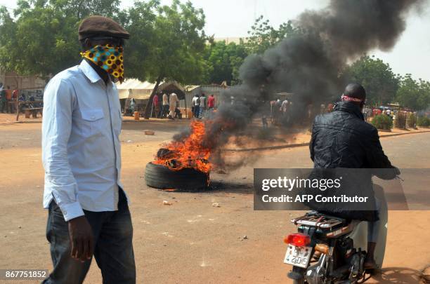 Man walks by as a motorcyclist drives past a burning tyre during clashes between protesters and police at a demonstration against the 2018 Finance...