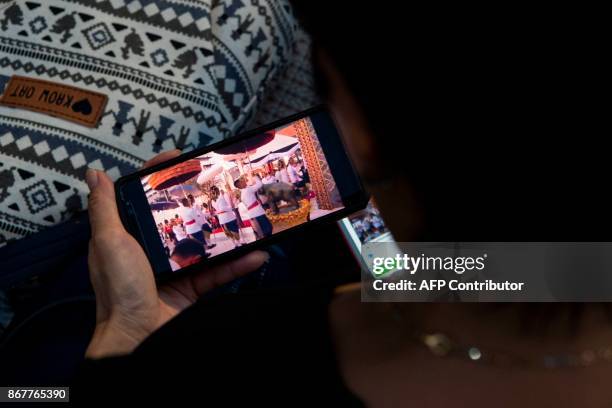 Mourner watches the ceremony on a mobile phone during the procession transferring the relics and ashes of the late Thai King Bhumibol Adulyadej from...