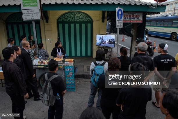 Crowd gathers at a corner to watch a funeral procession of the relics of the late Thai king Bhumibol Adulyadej on a TV set in Bangkok as they were...