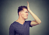 Man slapping hand on head having regrets isolated on gray background. Negative human emotion feeling