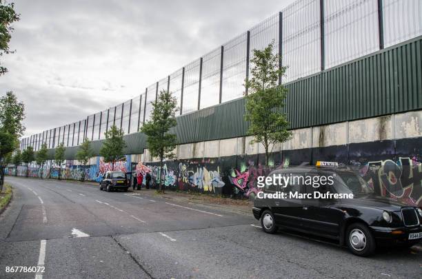 two black taxis and people in front of  the belfast wall separating catholics from protestants during day of autumn - the wall that divides belfast stock pictures, royalty-free photos & images