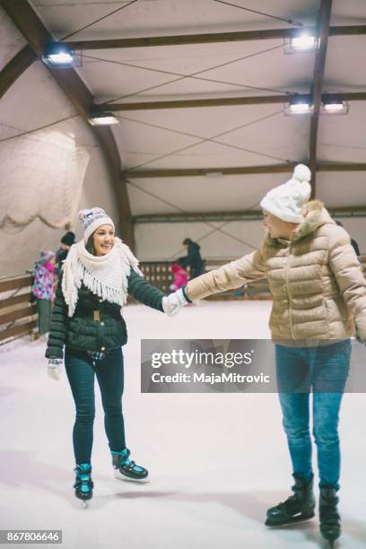 people, winter, friendship, sport and leisure concept - happy friends ice skating on rink outdoors - indoor skating stock pictures, royalty-free photos & images