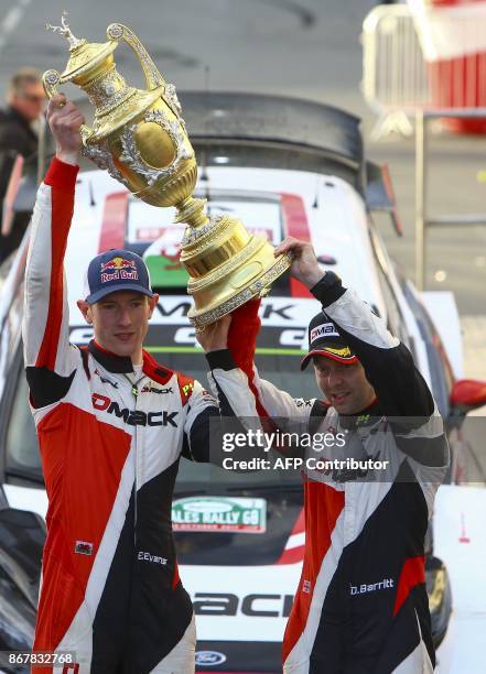 British pilot Elfyn Evans and co pilot Daniel Barritt of the M-Sport World Rally hold up their trophy as they celebrate in front of their Ford Fiesta...