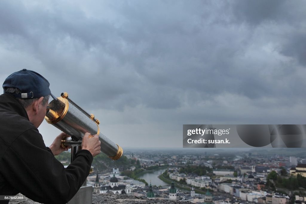 Senior man looking through binoculars of the city of Salzburg.