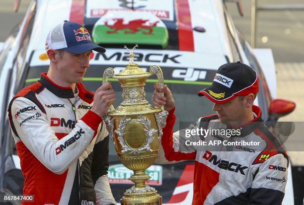 British pilot Elfyn Evans and co pilot Daniel Barritt of the M-Sport World Rally hold up their trophy as they celebrate in front of their Ford Fiesta...