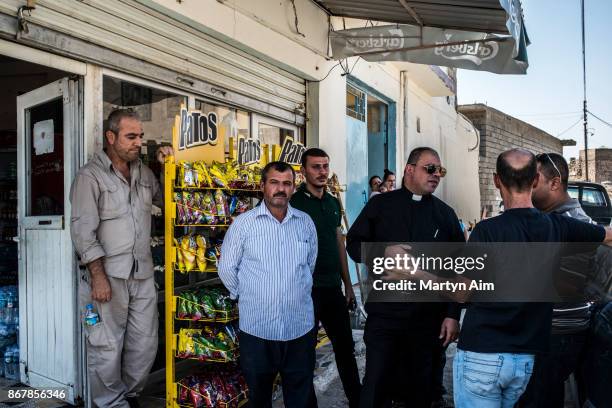 Chaldean Catholic Father Thadet talks with locals outside a reopened store in Karamles, a Christian town in northern Iraq, on September 8, 2017.