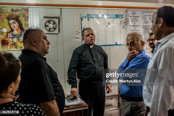 Father Thadet, the Chaldean Catholic priest of Karemles, talks with local residents in the Karemles Complex in Erbil, northern Iraq, on September 8,...