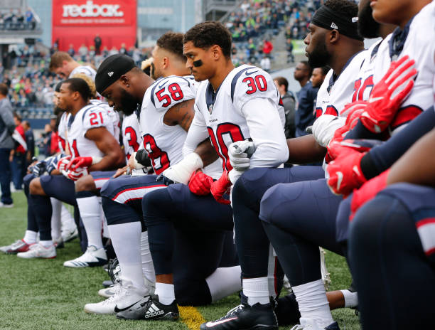 Members of the Houston Texans, including Kevin Johnson and Lamarr Houston, kneel during the national anthem before the game at CenturyLink Field on...