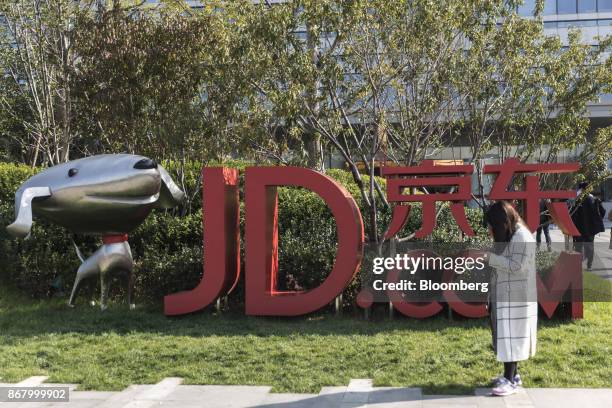 Woman stands next to signage incorporating the logo of JD.com Inc. And the company's mascot "Joy" at the company's headquarters in Beijing, China, on...