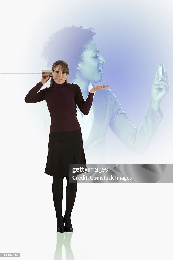 Woman listening to tin can on string and woman looking at cell phone
