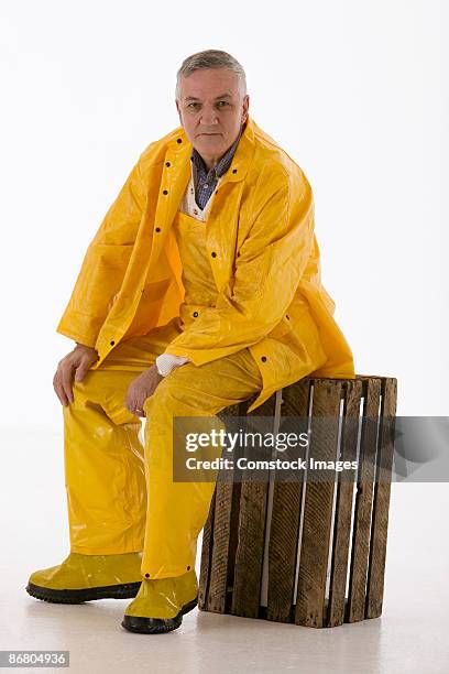 man in rain gear sitting on wooden crate - fisherman isolated stock pictures, royalty-free photos & images