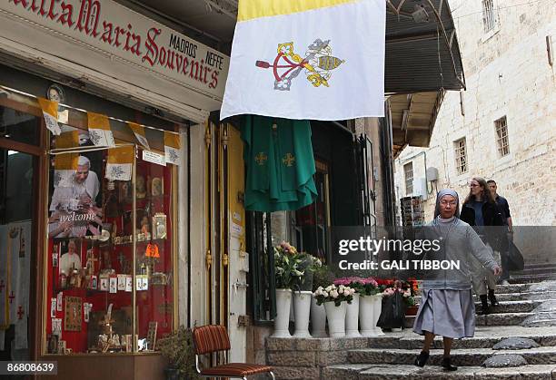 Catholic nun walks past the Vatican flag and a poster welcoming Pope Benedict XVI with the word "Welcome" written in several languages including...