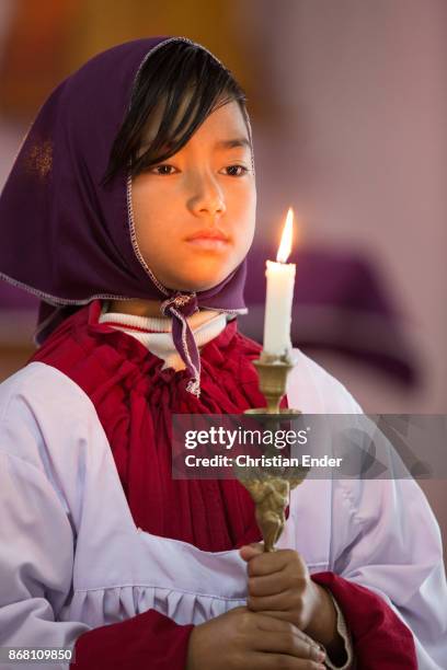 Kalimpong, India A young girl as a altar server with a tunicle is holding a candle while a ceremony inside a church in Kalimpong.