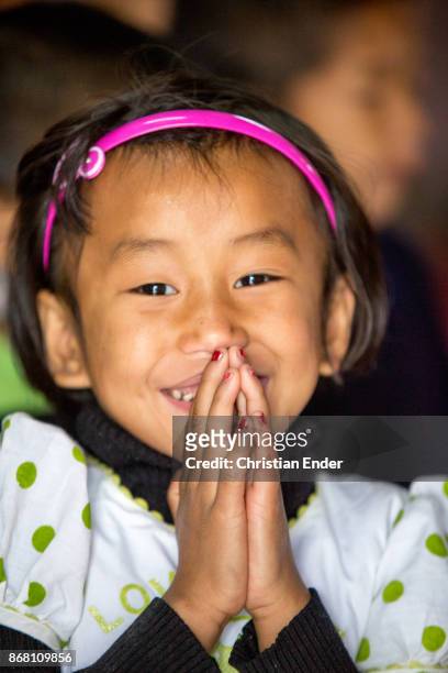 Kalimpong, India portrait of a young girl, who is smiling towards the camera while she hold up her hands to pray.