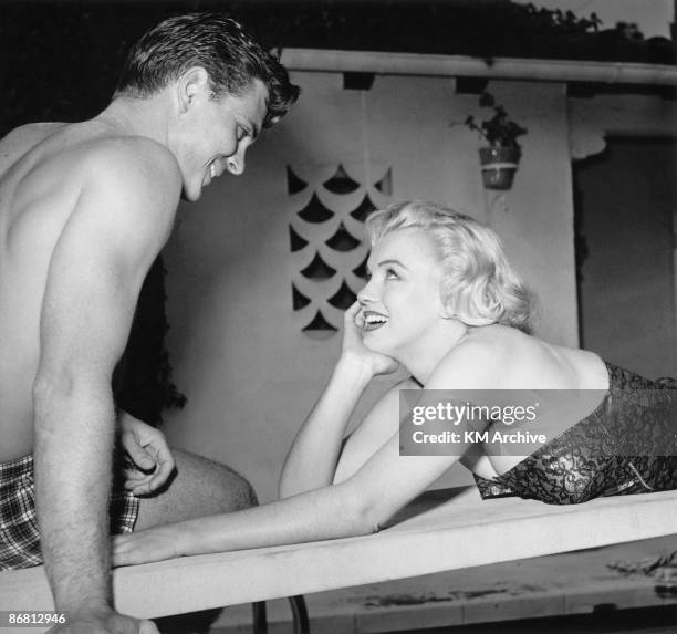 American actress Marilyn Monroe in a bathing suit and lying on her stomach, looks up to flirt with a friend at the pool, Hollywood, California, 1950.