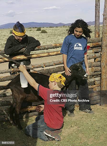 Brett watches Colton milking the goat as Guylan holds him still in KID NATION on the CBS Television Network.