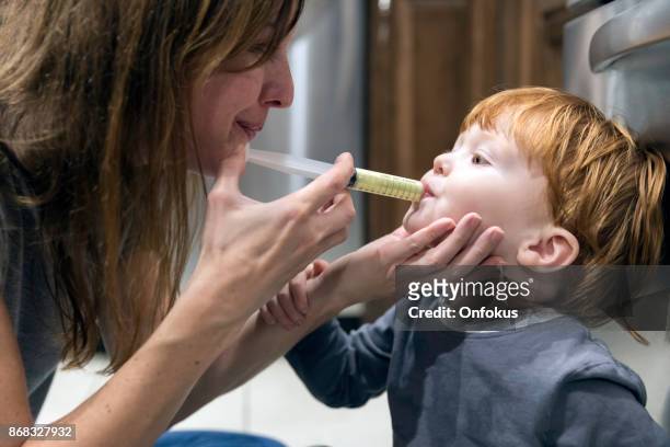 mother giving penicillin medicine to his sick baby boy - hand over mouth stock pictures, royalty-free photos & images