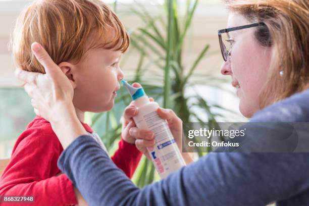 la mamma pulisce il naso del bambino con soffiante e spray nasale salino - flebo salina foto e immagini stock