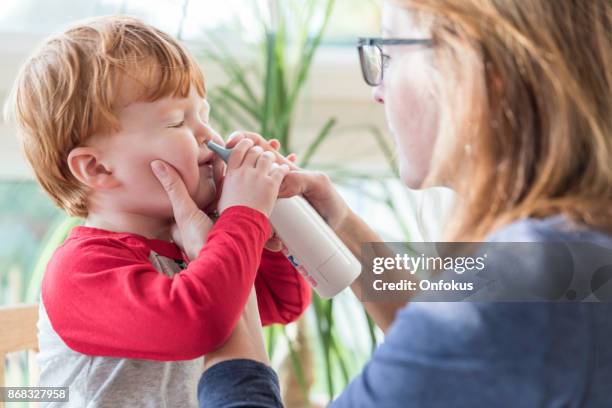 mom は、送風機と生理食塩水の鼻スプレー赤ちゃんの鼻をクリーンアップします。 - 生理食塩水 ストックフォトと画像