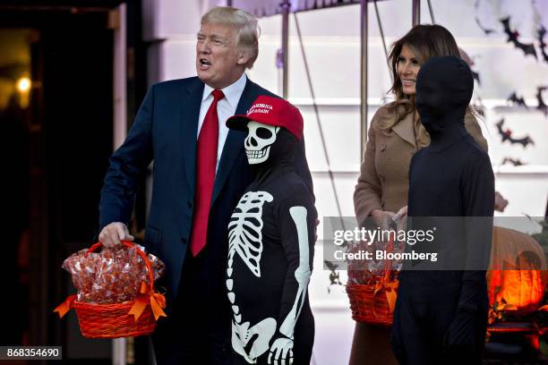 President Donald Trump stands with a child wearing a "Make America Great Again" hat and skeleton costume next to U.S. First Lady Melania Trump,...