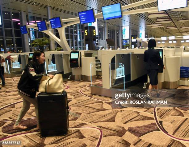 Passenger pushes her luggage towards an automated check-in booth at the newly-opened Singapore Changi Airport's Terminal 4 in Singapore on October...