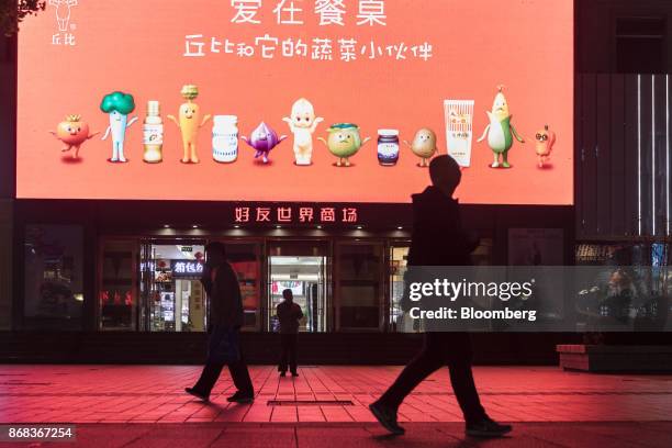 Pedestrians walk past an illuminated advertisement for Kewpie Corp. Products displayed on a screen at the Beijing Haoyou World Shopping Mall on...