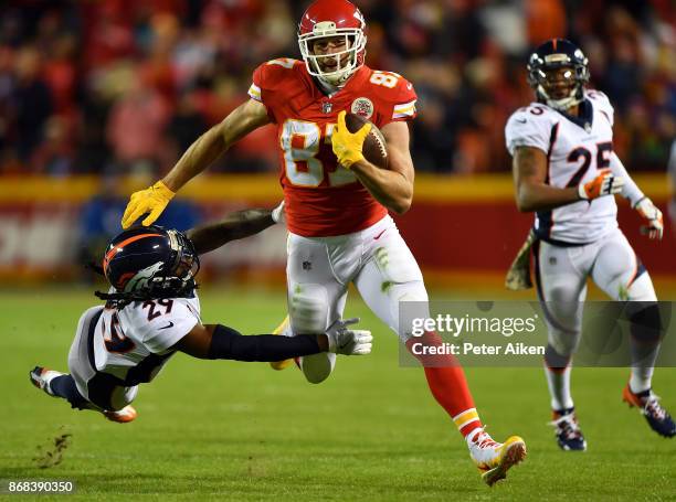 Tight end Travis Kelce of the Kansas City Chiefs carries the ball after making a catch as free safety Bradley Roby of the Denver Broncos defends...