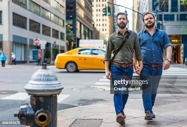 walking mature adult gay men crossing the street while holding hands in new york - holding hands in car stock pictures, royalty-free photos & images