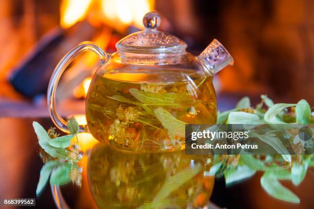 teapot with lime tea and linden flowers on the background of the fireplace - linde bladverliezende boom stockfoto's en -beelden
