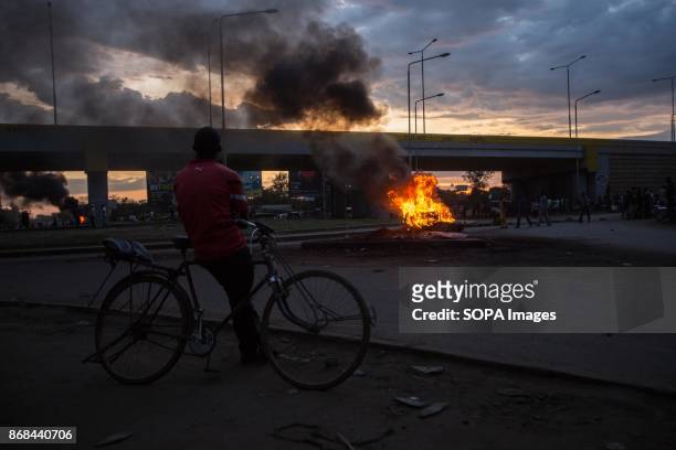 Man on his bicycle seen looking at the fire during a protest in Kisumu. After the IEBC announced the new president elect of Kenya, it sparked...