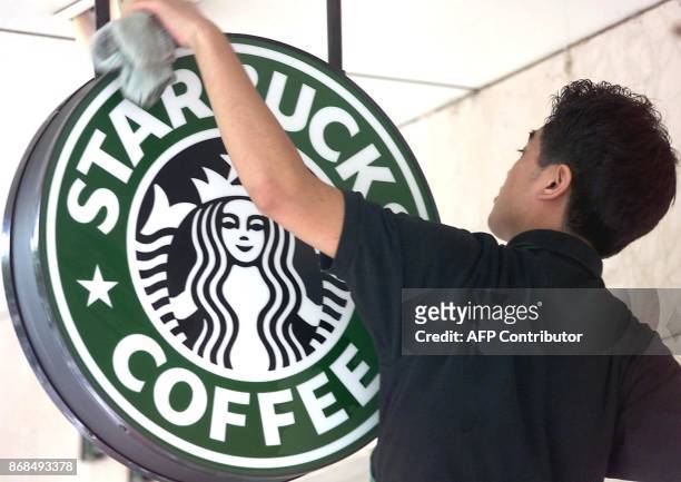 Worker cleans the sign outside a global coffee franchise Starbucks outlet in Beijing 25 October 2000. Coffee was introduced to China in the 1920s,...