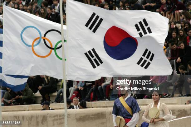 Dancers dressed in traditional costume stand near the Greek, Olympic and South Korean flags during the handover ceremony of the Olympic flame for the...